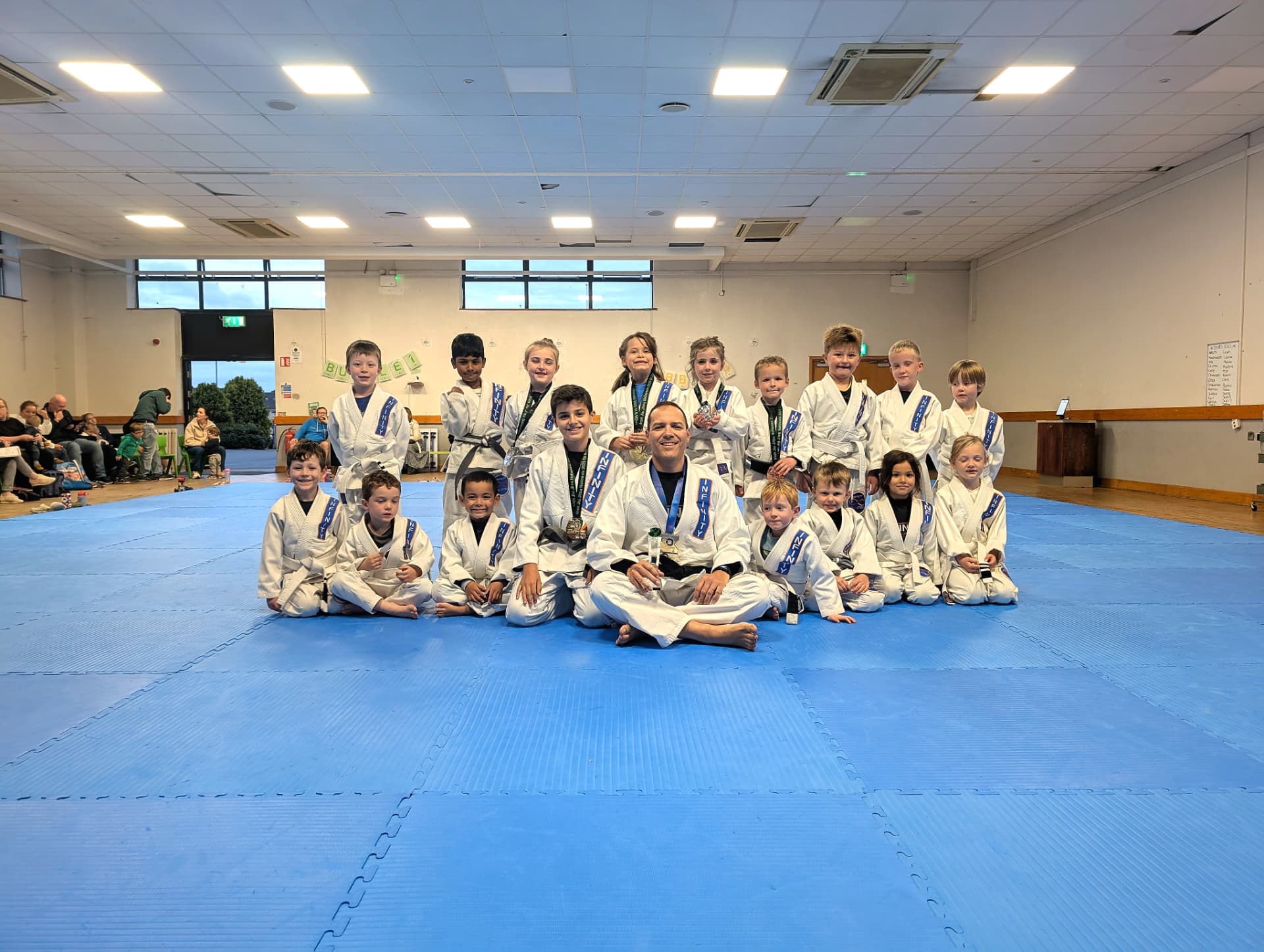 Professor Fabiano sitting on the mats with a group of young Infinity students holding their medals